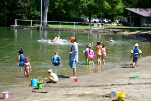 kids and adults playing in a pond with a beach.